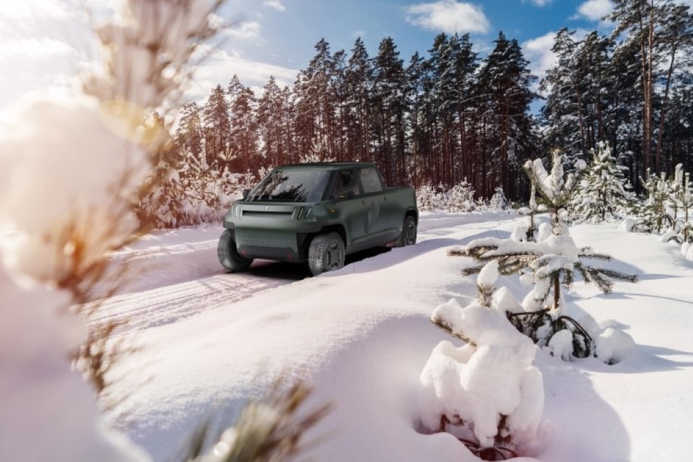 Green TELO truck driving through a snow covered road with pine trees in the background.