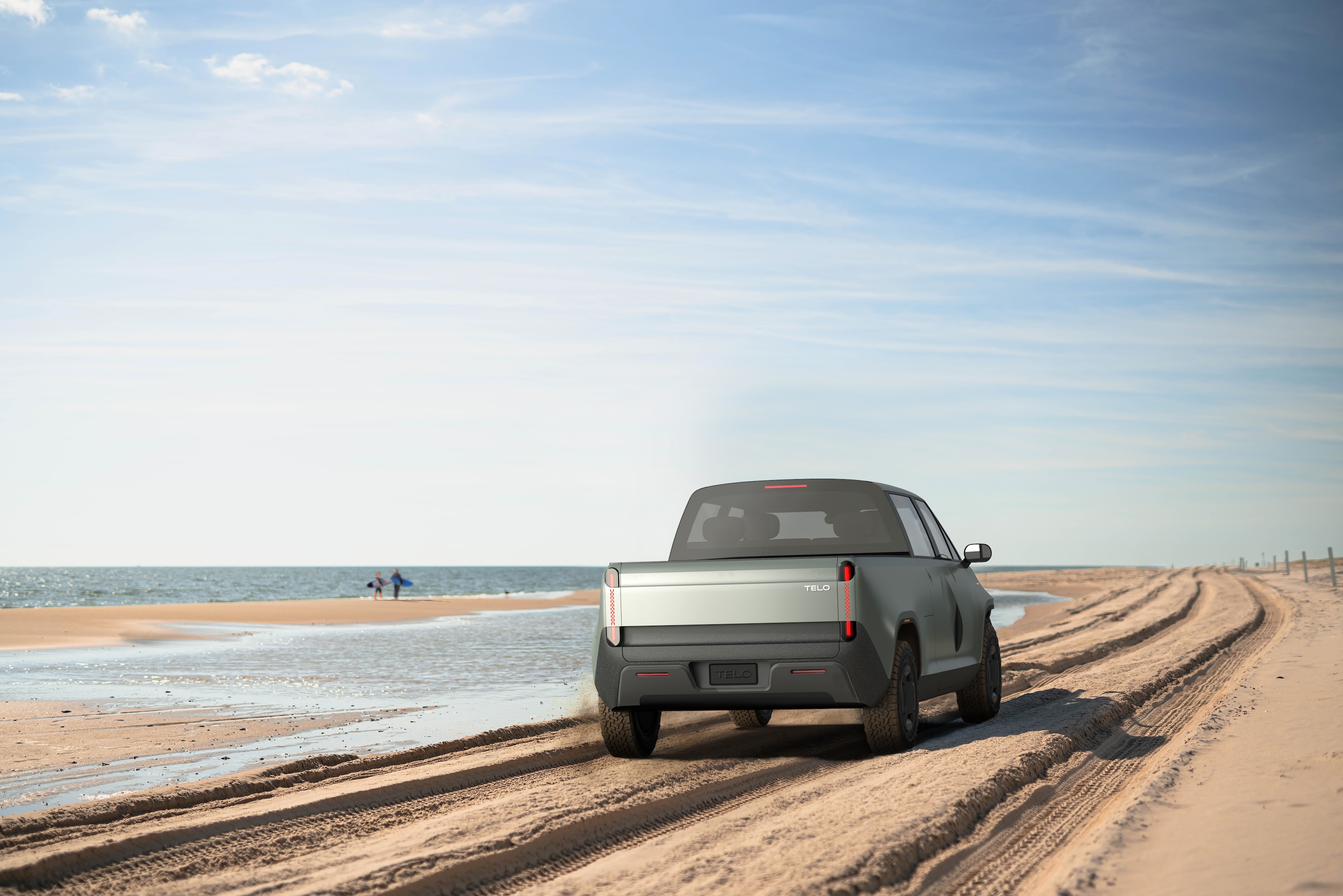 TELO truck from behind driving on the beach with surfers walking in the distnace.