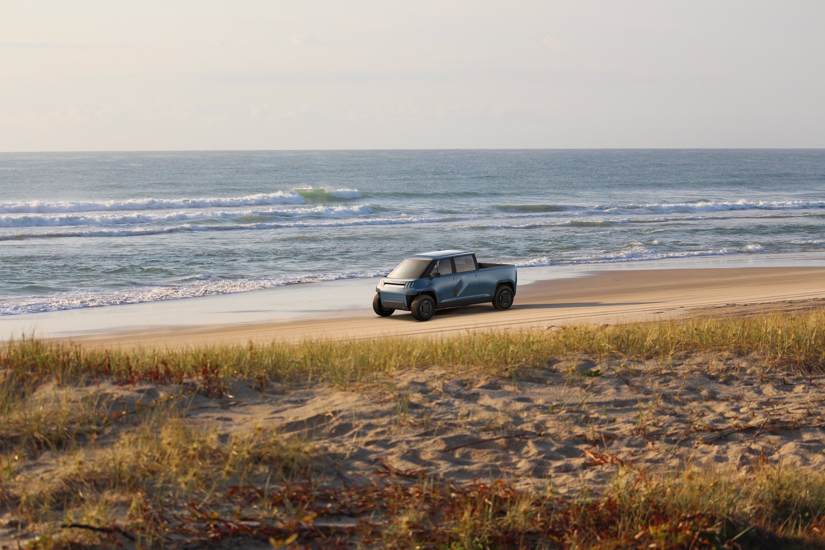 TELO truck from a distance driving on the beach with the ocean waves lapping in the background.