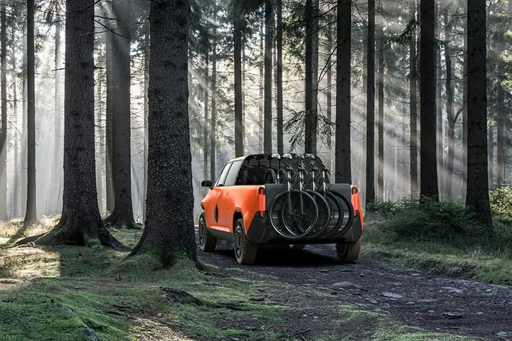 An orange TELO Truck from behind with four mountain bikes mounted on the back driving through a forest.